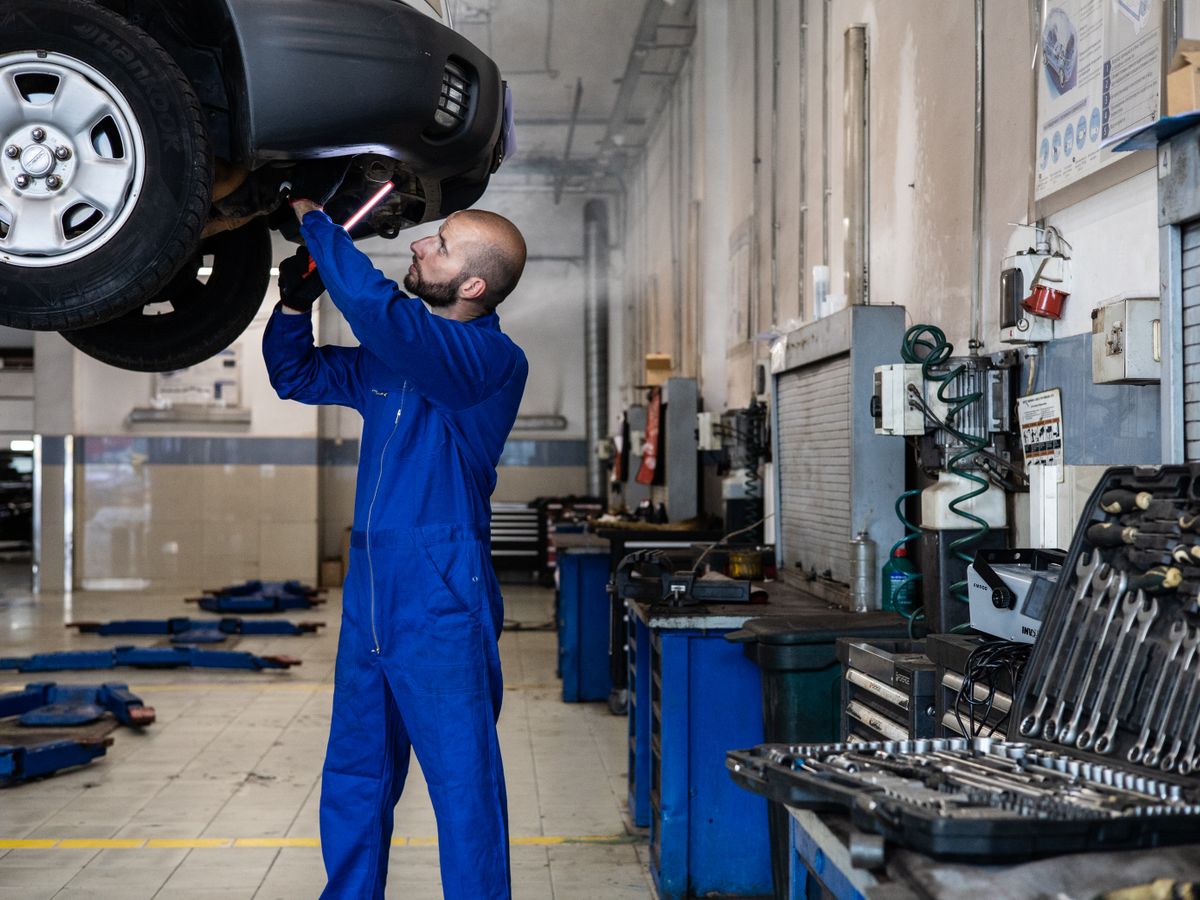 Mecânico a inspecionar um carro elevado numa oficina